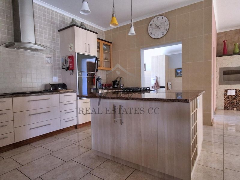 Spacious kitchen featuring a central island with granite countertops, built-in oven, gas hob, extractor fan, and tiled finishes, adjacent to a built-in fireplace.
