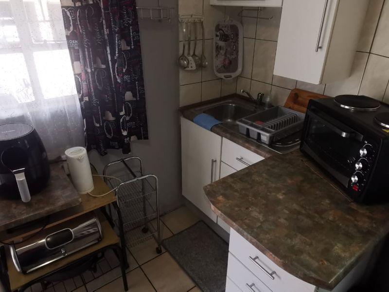 Compact kitchen featuring built-in cabinetry, laminate countertops, a stainless steel sink, and tiled backsplash, offering a functional prep area.