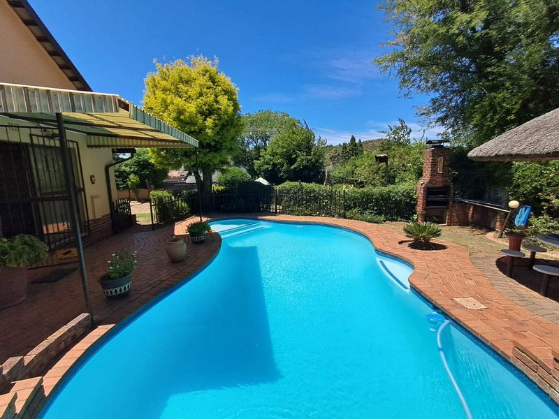 Outdoor pool area featuring a swimming pool, brick paved surround, built-in braai, and a thatched lapa, perfect for outdoor entertaining.