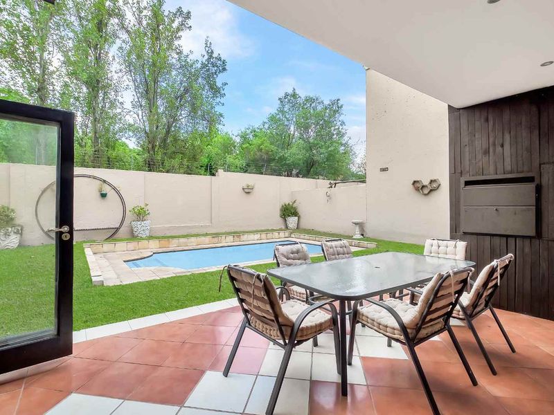 Covered patio area featuring a built-in braai, tiled flooring, and direct access to a private garden with a swimming pool.