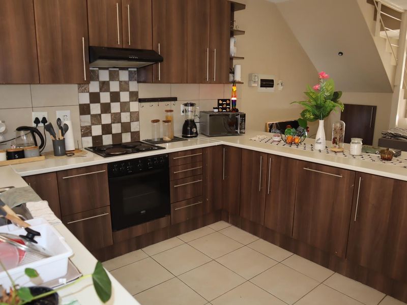 A functional kitchen featuring dark wood-look cabinetry, stone countertops, a built-in oven with hob, and a tiled backsplash, with an open-plan layout.