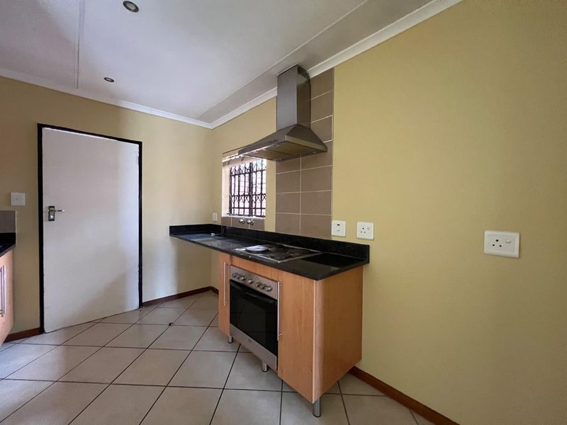 A functional kitchen featuring built-in oven, hob, extractor fan, granite countertops, and tiled flooring, offering a clean and practical workspace.