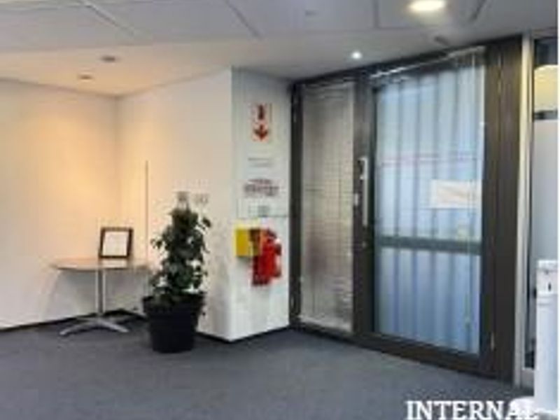 A professional office entrance area featuring carpeted flooring, suspended ceiling tiles with recessed lighting, and a secure glass door with integrated security bars.
