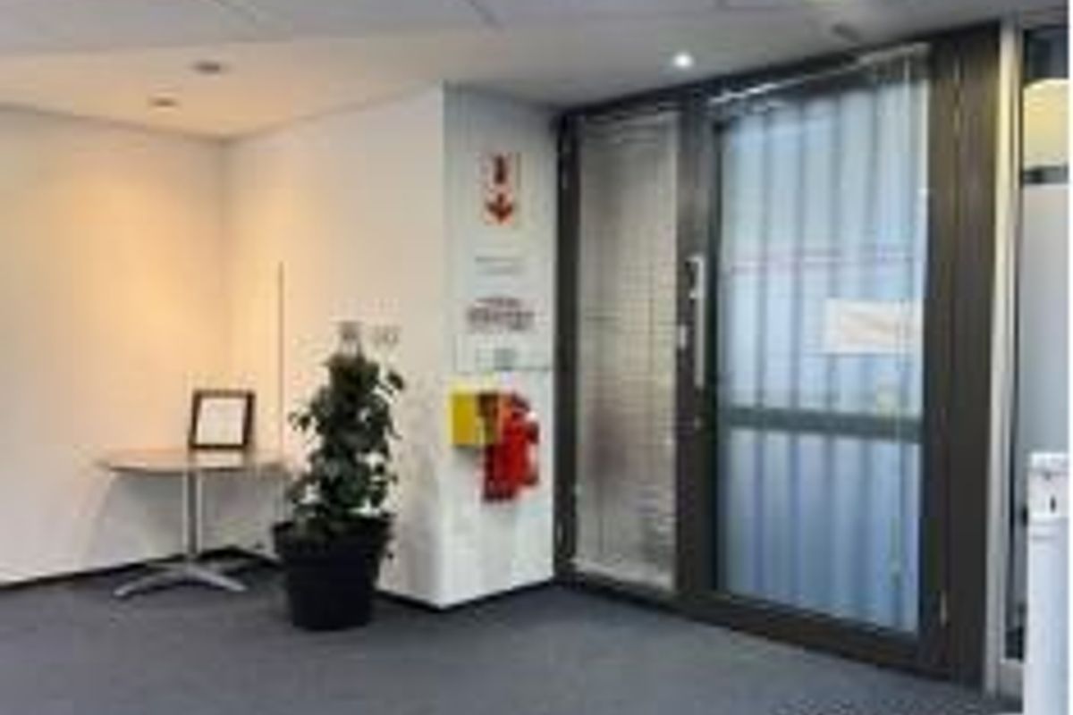 A professional office entrance area featuring carpeted flooring, suspended ceiling tiles with recessed lighting, and a secure glass door with integrated security bars.