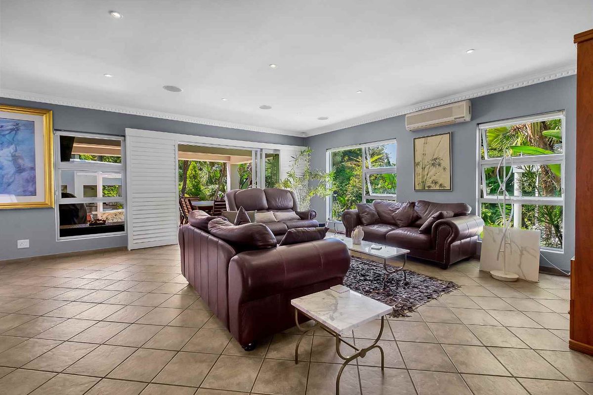 Spacious living room featuring tiled flooring, recessed lighting, crown molding, and large windows with garden views, leading out to a covered patio area.