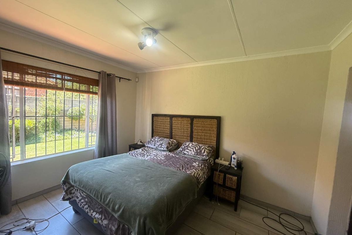 A bedroom featuring tiled flooring, a window with security bars, and a central ceiling light fixture, offering a functional and well-lit living space.