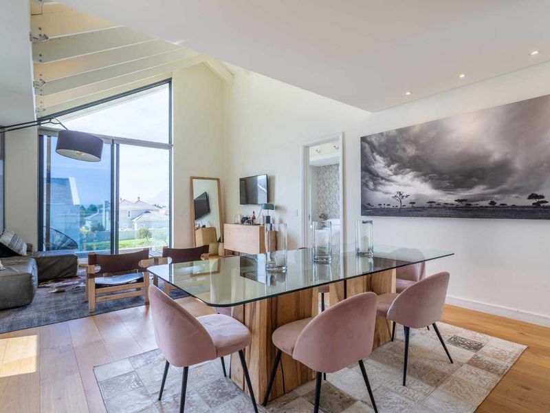 Spacious open-plan living and dining area featuring vaulted ceilings with exposed rafters, hardwood flooring, and large sliding glass doors providing ample natural light.