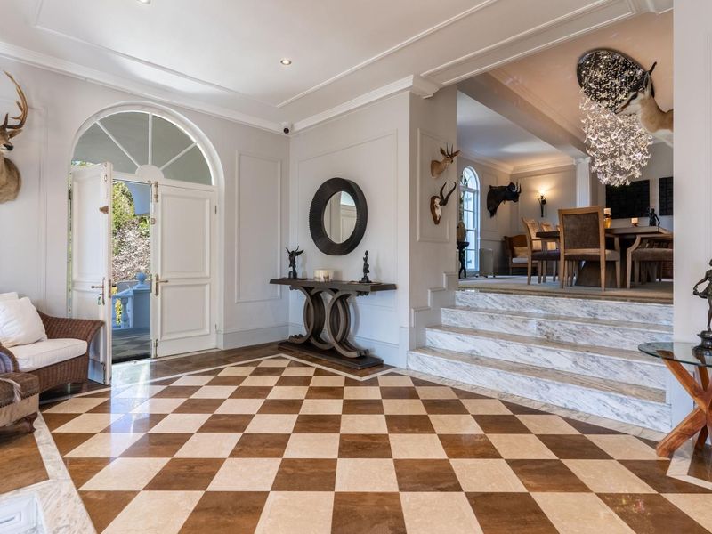 Elegant grand entrance hall featuring checkered marble flooring, an arched double door, and a marble staircase leading to the dining area.
