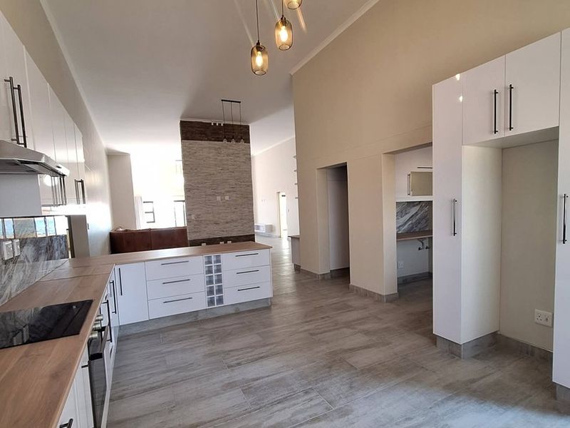 Modern open-plan kitchen featuring sleek white cabinetry, stone-look tile flooring, and a striking stone feature wall, creating a bright and contemporary living space.