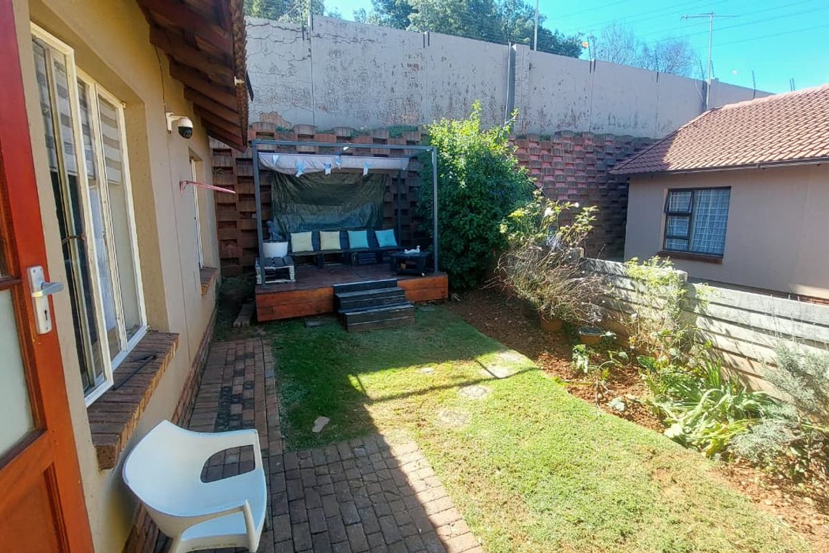 A rear garden area featuring a raised timber deck, paved walkway, and a concrete retaining wall boundary.