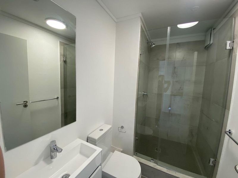 A clean and modern bathroom featuring a vanity basin, toilet, and a glass-enclosed shower with neutral wall tiling.