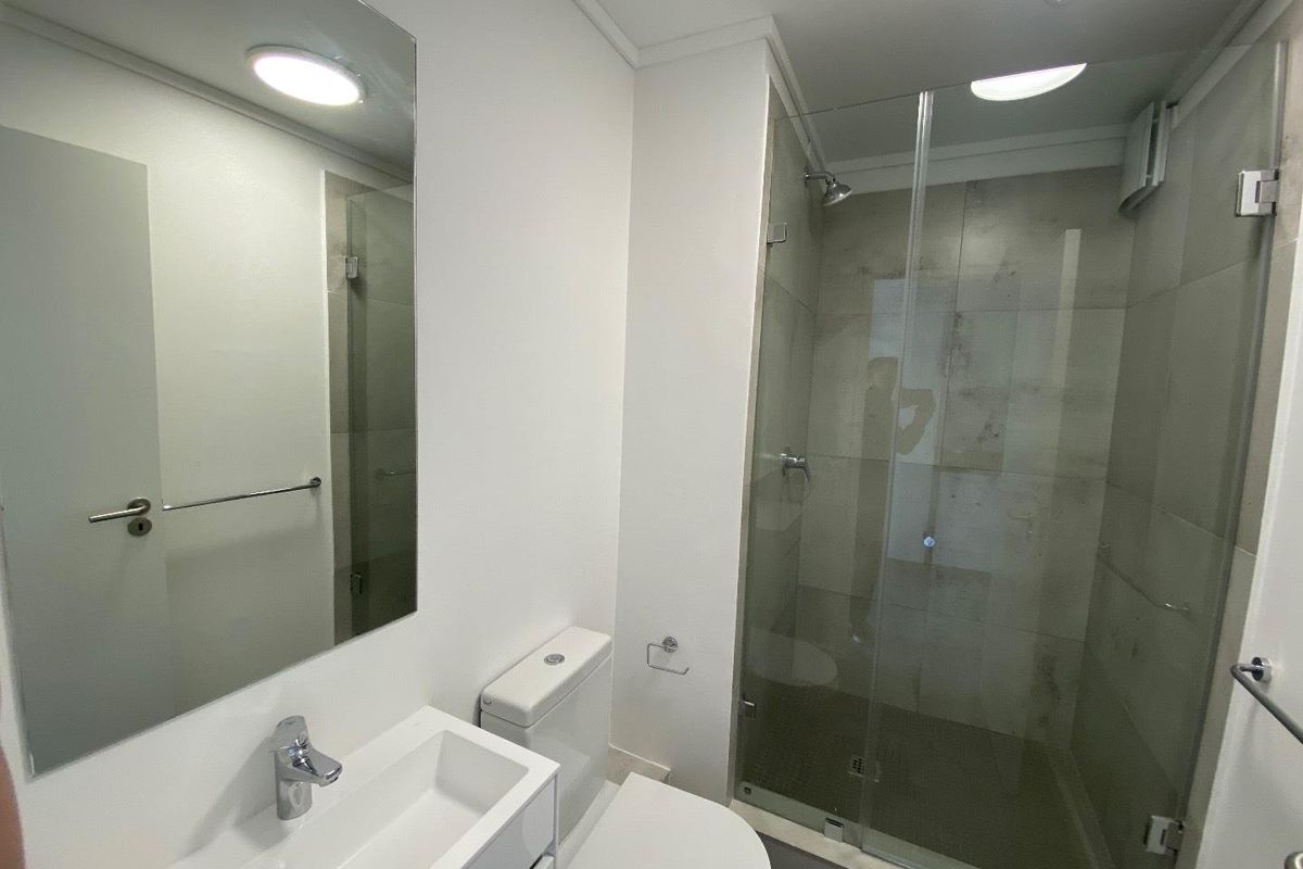 A clean and modern bathroom featuring a vanity basin, toilet, and a glass-enclosed shower with neutral wall tiling.