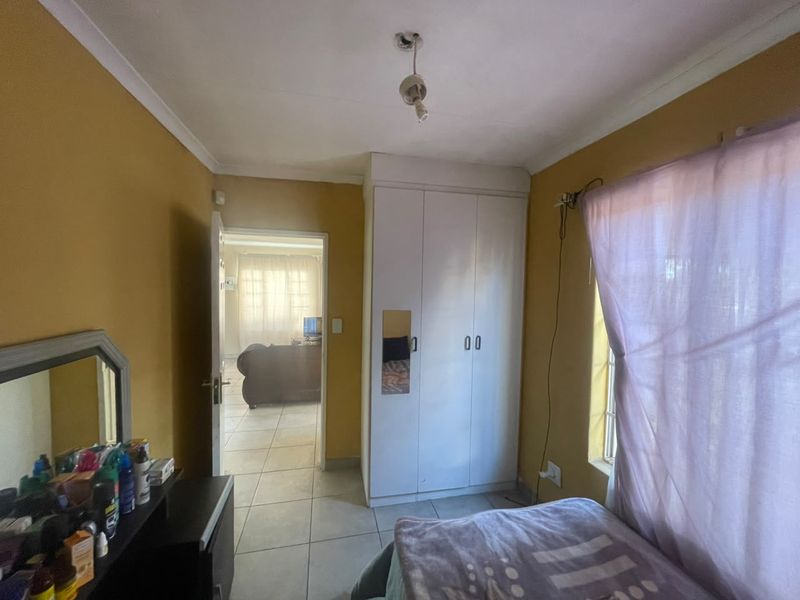 A bedroom featuring tiled flooring, a built-in wardrobe, and cove cornicing, with an adjacent view into the living area.