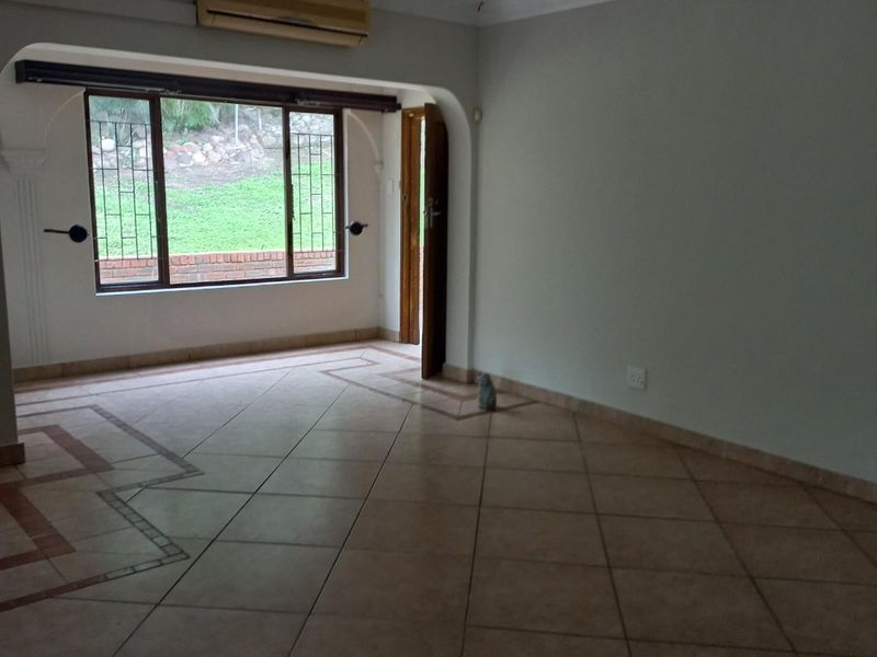An empty, spacious living area featuring tiled floors, an archway, and a wall-mounted air conditioning unit with views of the garden.