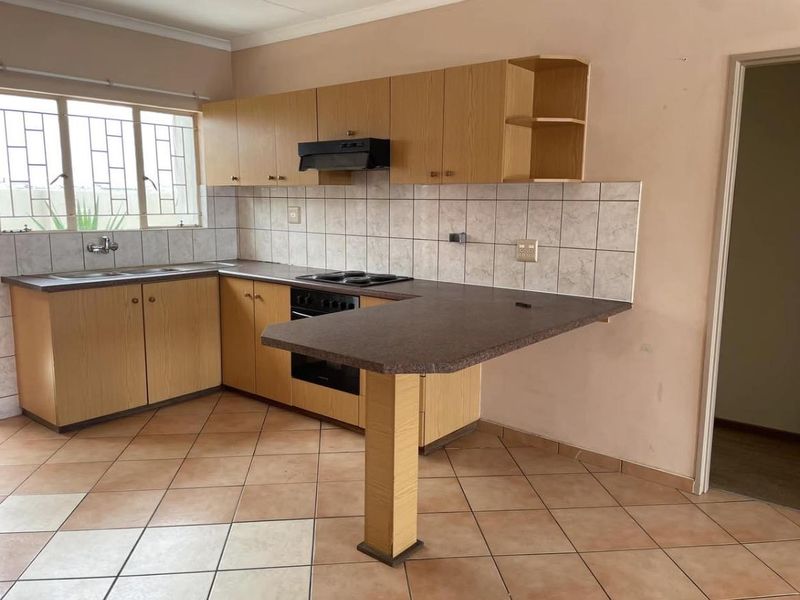 A functional kitchen featuring laminate cabinetry, a built-in oven with hob, extractor fan, and a breakfast bar counter, finished with ceramic floor tiles.