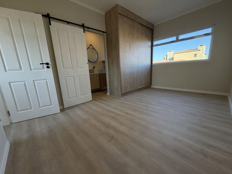 A bright, empty bedroom featuring modern laminate flooring, a large built-in wardrobe, and a sliding barn door leading to an en-suite bathroom.