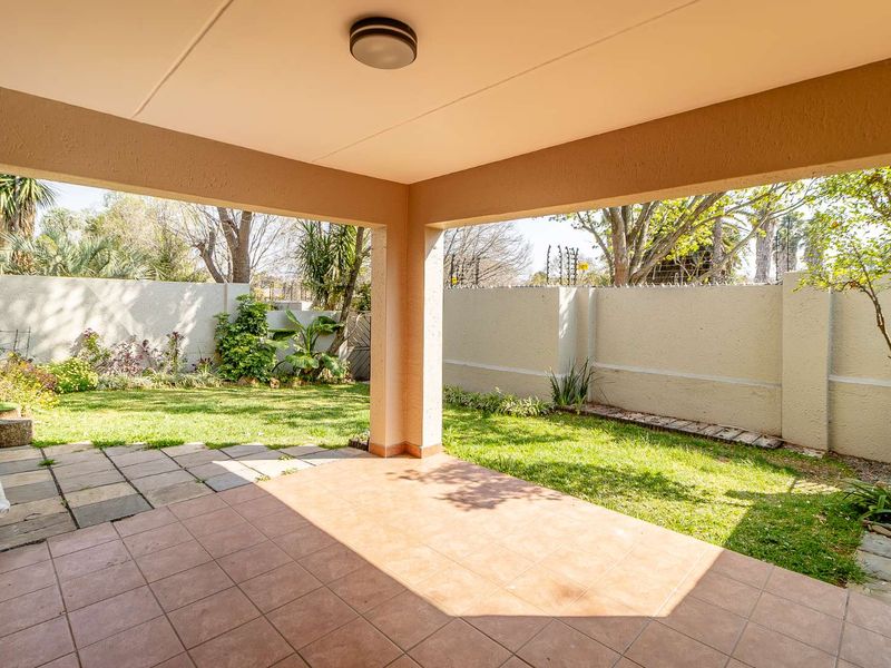 A covered patio area featuring tiled flooring, overlooking a private garden enclosed by perimeter walls with electric fencing.