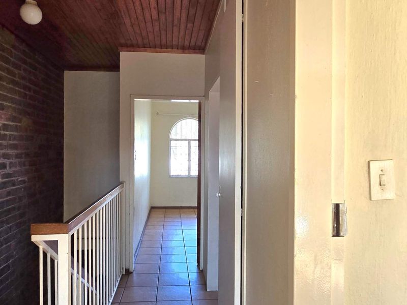 A hallway featuring exposed brickwork, a timber-paneled ceiling, and tiled flooring, leading towards an arched window at the end of the passage.