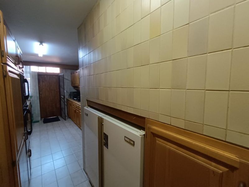 A dated kitchen featuring traditional wooden cabinetry, tiled wall splashbacks, and tiled flooring, offering a functional layout with potential for modern renovation.