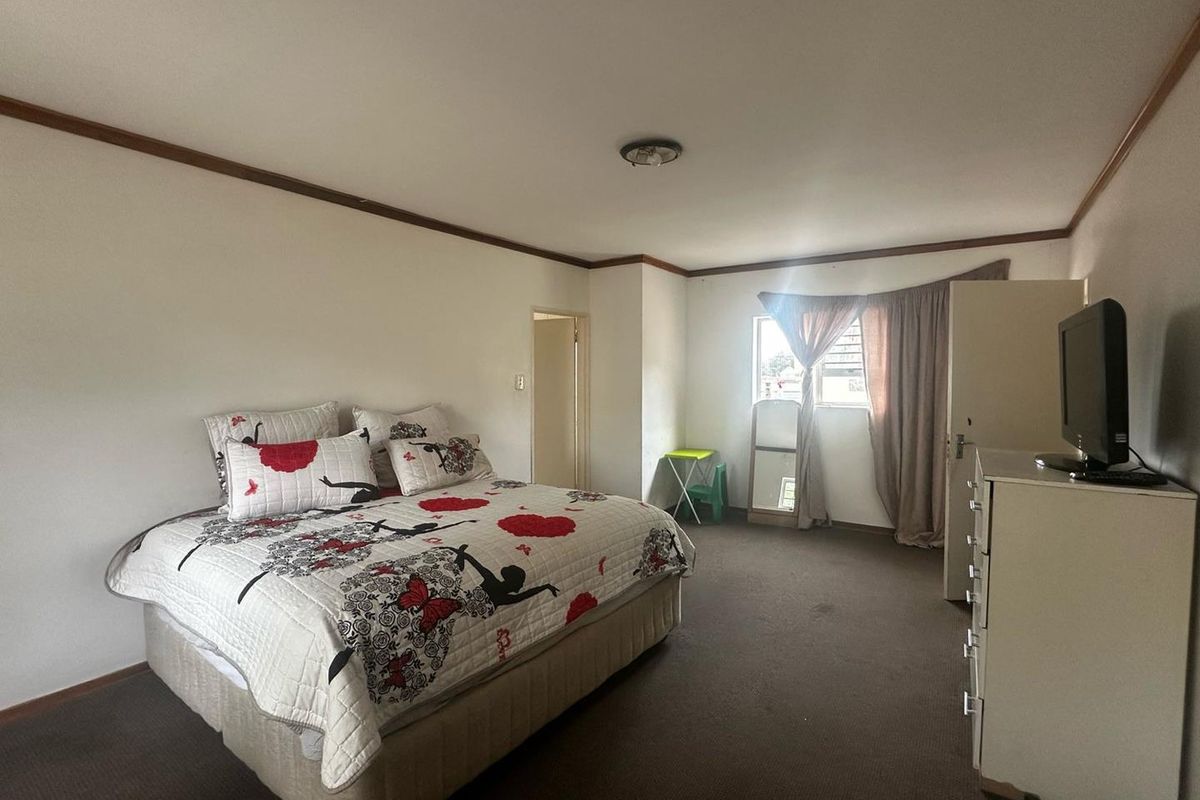 A spacious bedroom featuring neutral walls, carpeted flooring, and a window with curtain treatments.