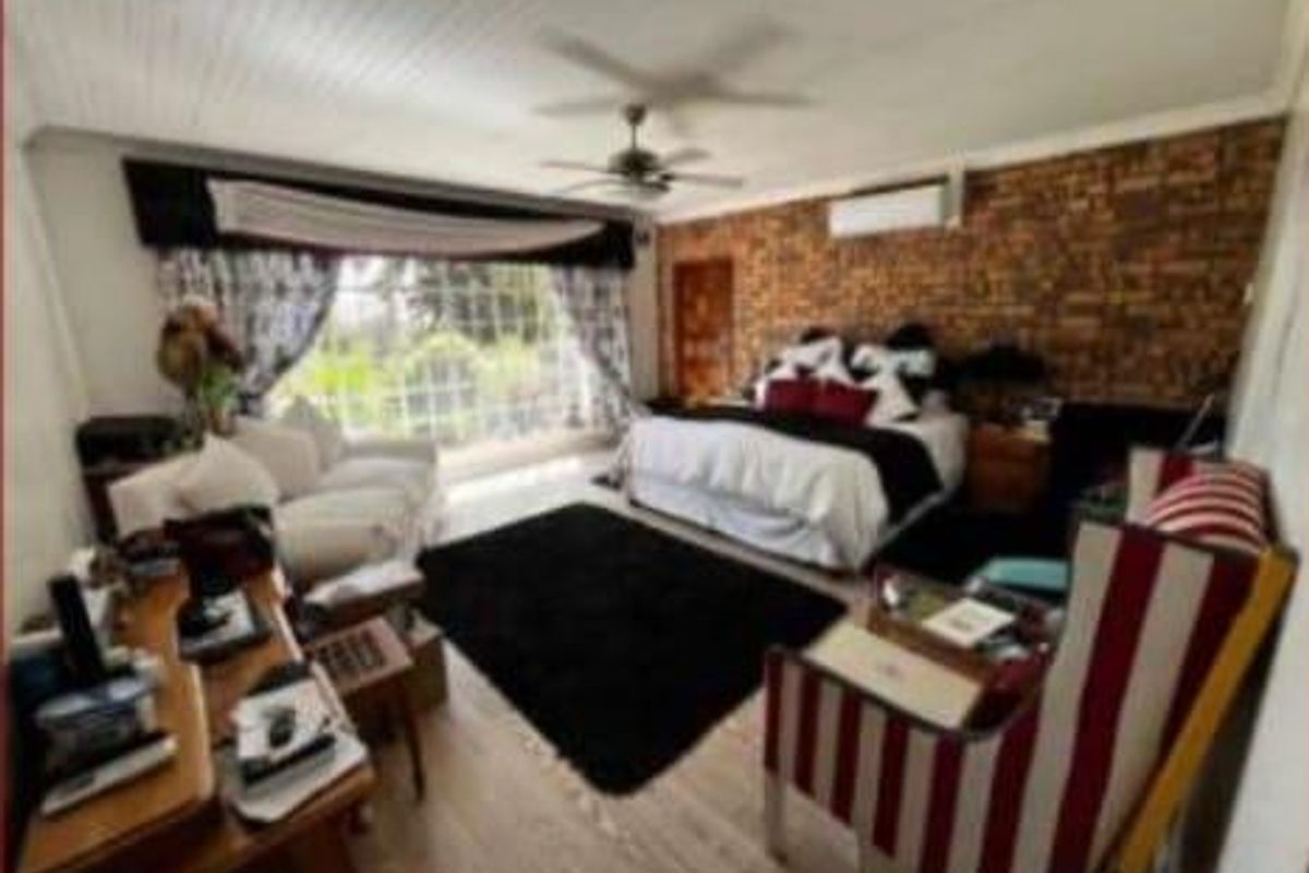 Spacious bedroom featuring an exposed brick feature wall, ceiling fan, split-system air conditioning, and large windows providing natural light.