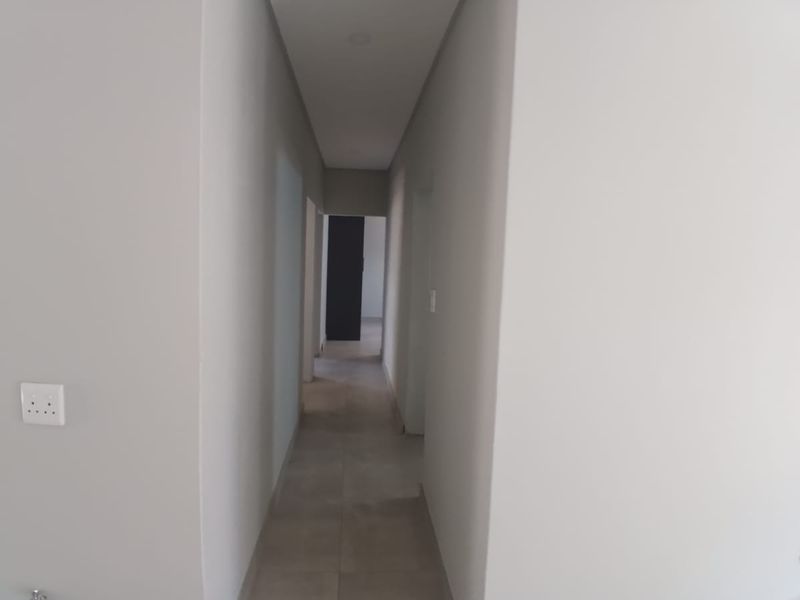 A clean, minimalist hallway featuring neutral wall tones, tiled flooring, and recessed ceiling lighting, providing a bright and seamless transition between rooms.