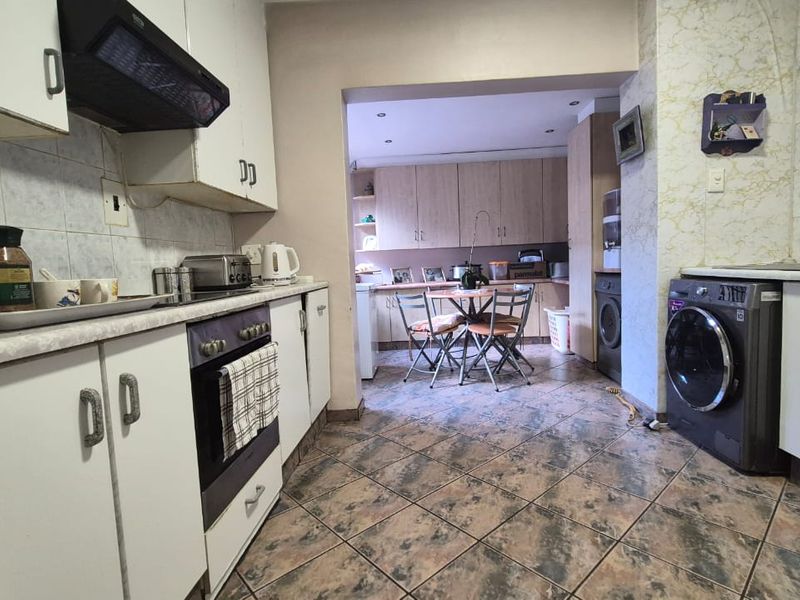 Open-plan kitchen and dining area featuring built-in cabinetry, integrated oven and hob, tiled flooring, and a dedicated laundry space with plumbing connections.