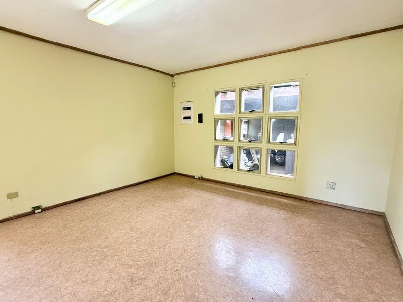 An empty office space featuring vinyl flooring, a multi-pane window, and a wall-mounted electrical distribution board.