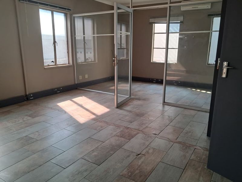 An empty office space featuring glass partition walls, tiled flooring, and an integrated air conditioning unit, suitable for a professional workspace.