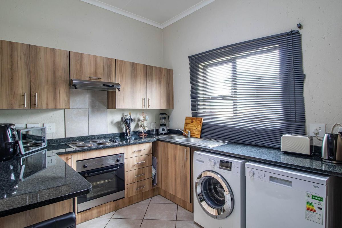 A functional kitchen featuring wood-look cabinetry, granite countertops, a built-in oven with extractor fan, and dedicated space for laundry appliances.