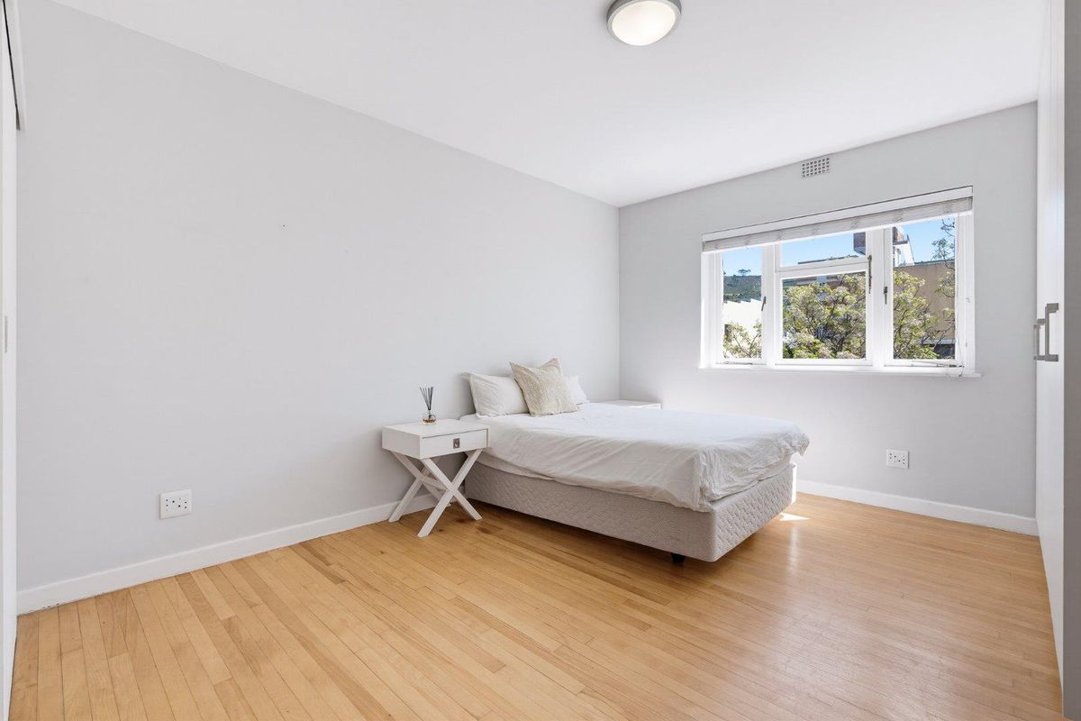 A bright bedroom featuring light hardwood flooring, a built-in wardrobe, and a window providing natural light.