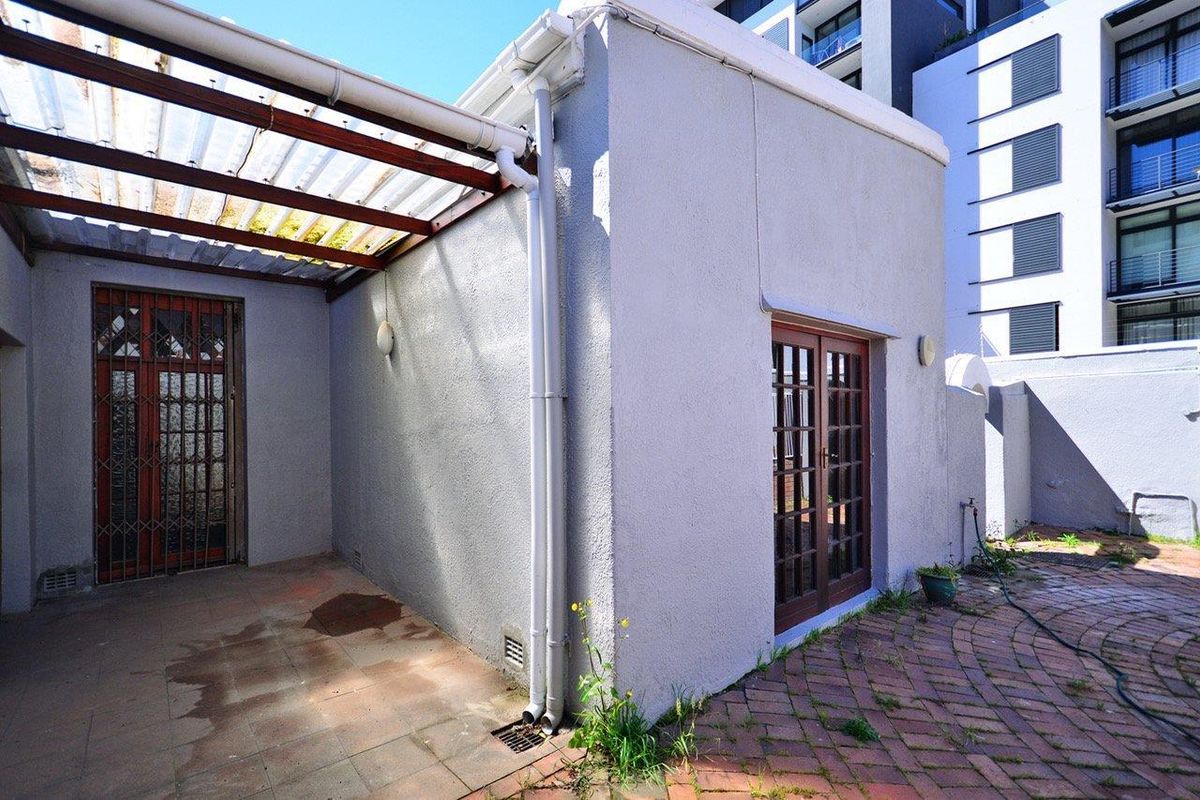 Rear exterior area featuring a paved patio, a covered pergola structure, and access via timber-framed french doors and a security gate.