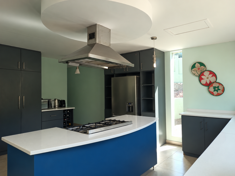 Modern kitchen featuring dark blue cabinetry, a central island with a gas cooktop, stainless steel extractor fan, and stone countertops.