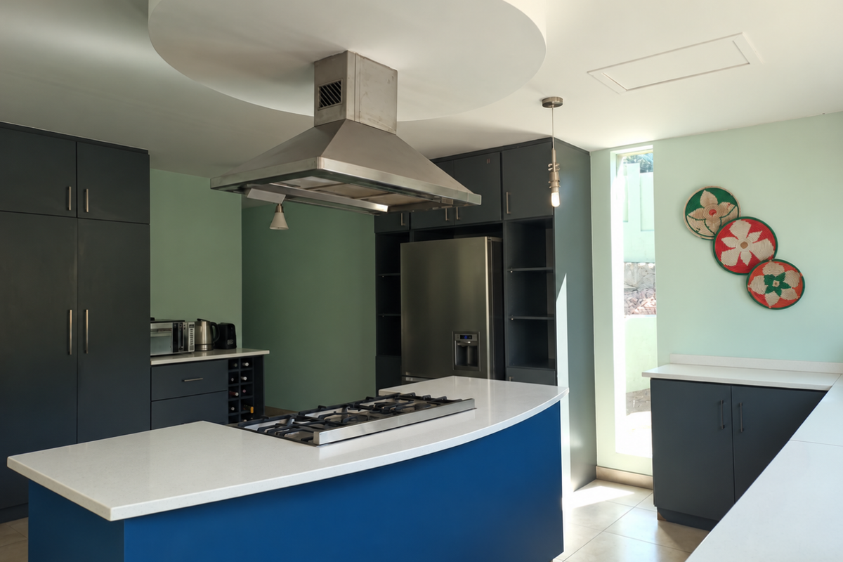 Modern kitchen featuring dark blue cabinetry, a central island with a gas cooktop, stainless steel extractor fan, and stone countertops.