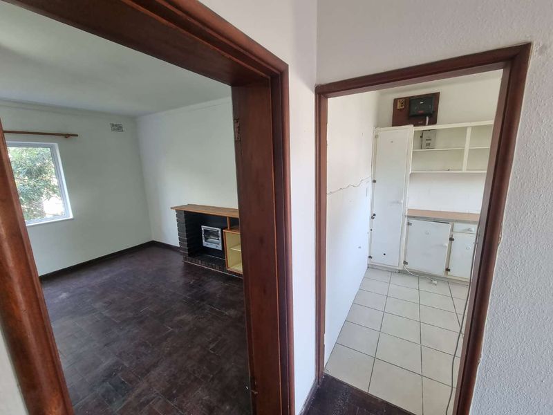 A view from the hallway looking into a living area with a brick fireplace and a kitchen featuring built-in cabinetry and tiled floors.