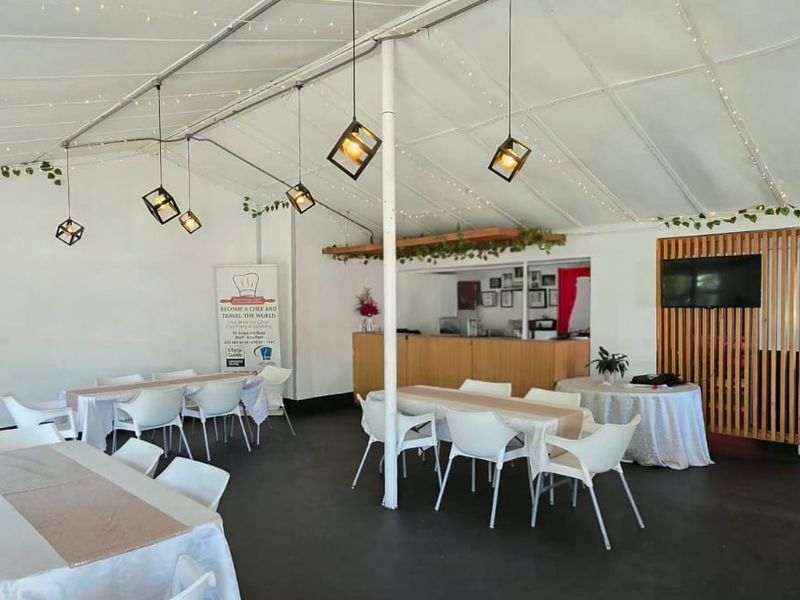 A covered outdoor event space featuring a fixed bar counter, timber slat screening, and a high-pitched fabric roof structure with pendant lighting.