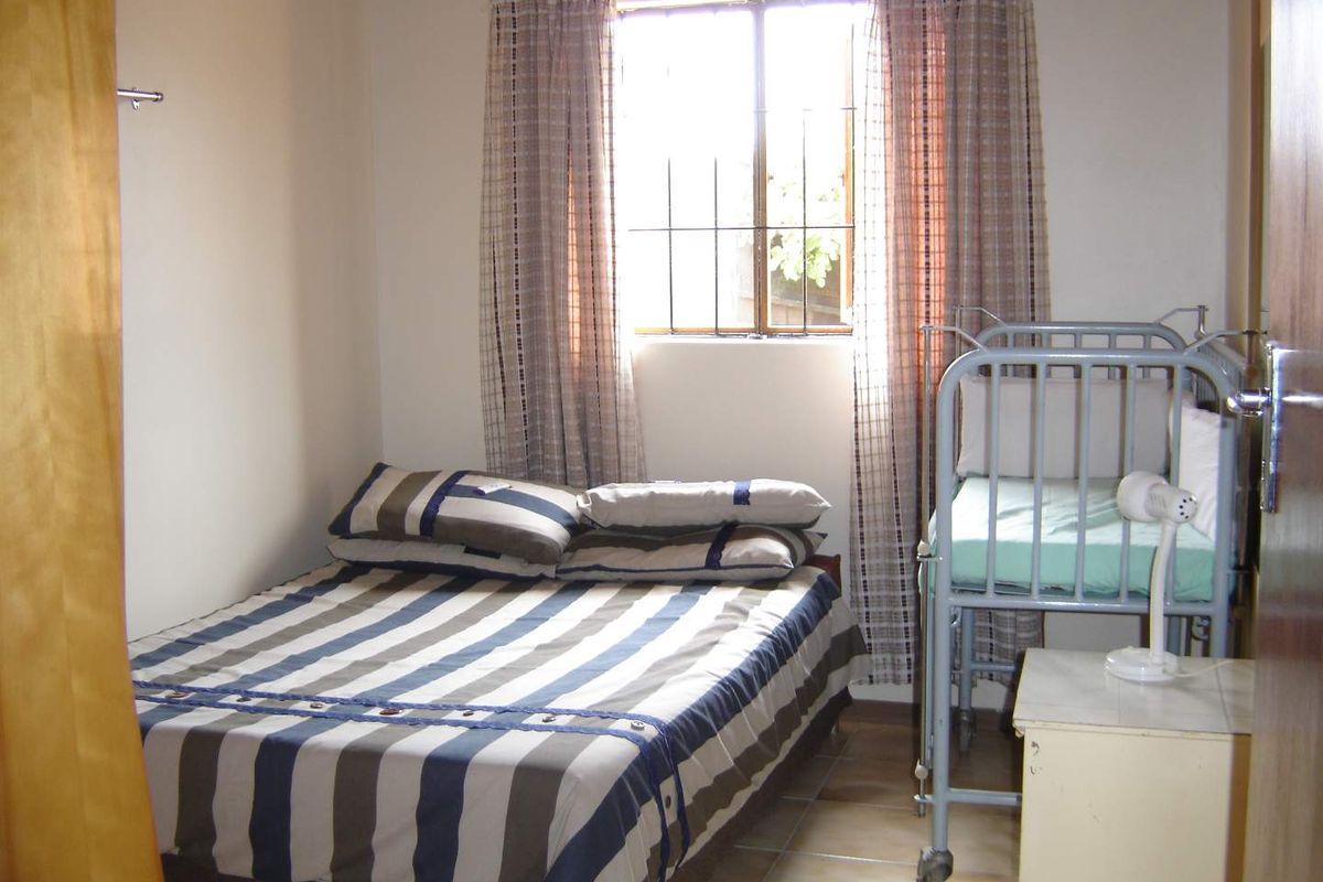 A functional bedroom featuring tiled flooring and a window with security bars, providing natural light and a practical layout.