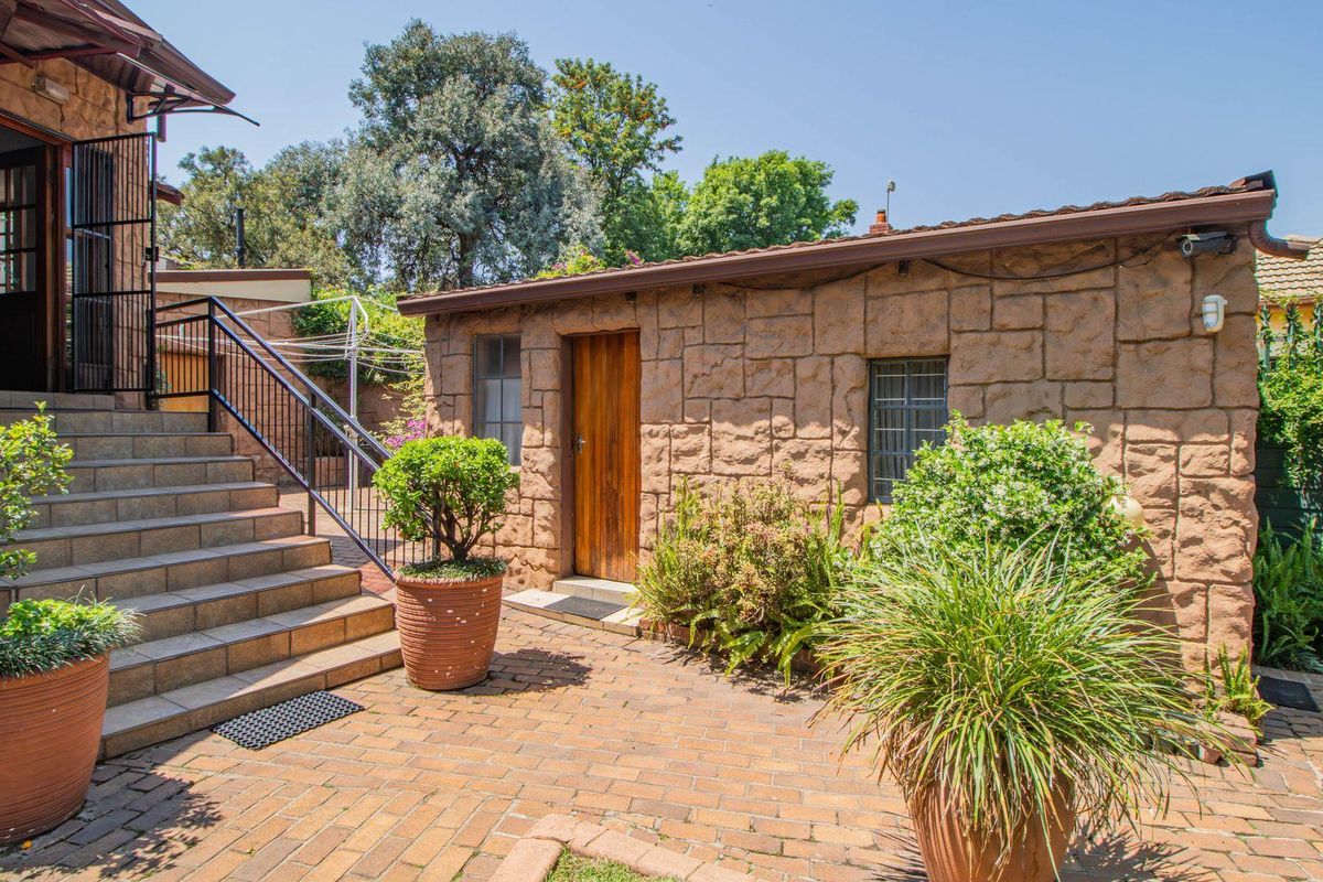 A paved courtyard area featuring a stone-clad outbuilding, external staircase with metal railings, and established garden greenery.