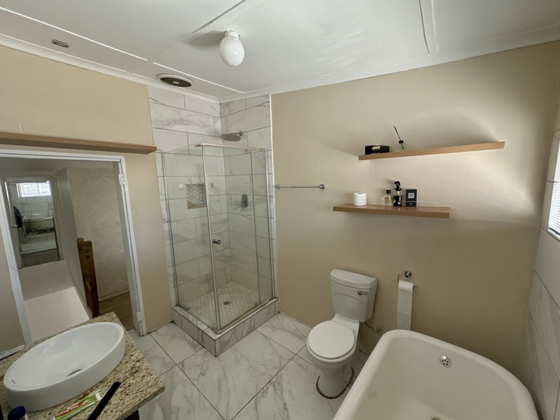 Modernized bathroom featuring a glass shower enclosure, marble-look tiling, granite vanity countertop, and a freestanding bathtub with floating timber shelving.