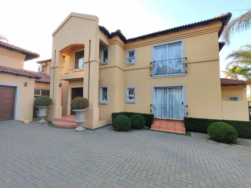 A well-maintained double-storey residential property featuring a paved driveway, tiled roof, and wrought iron balcony railings on the upper level.