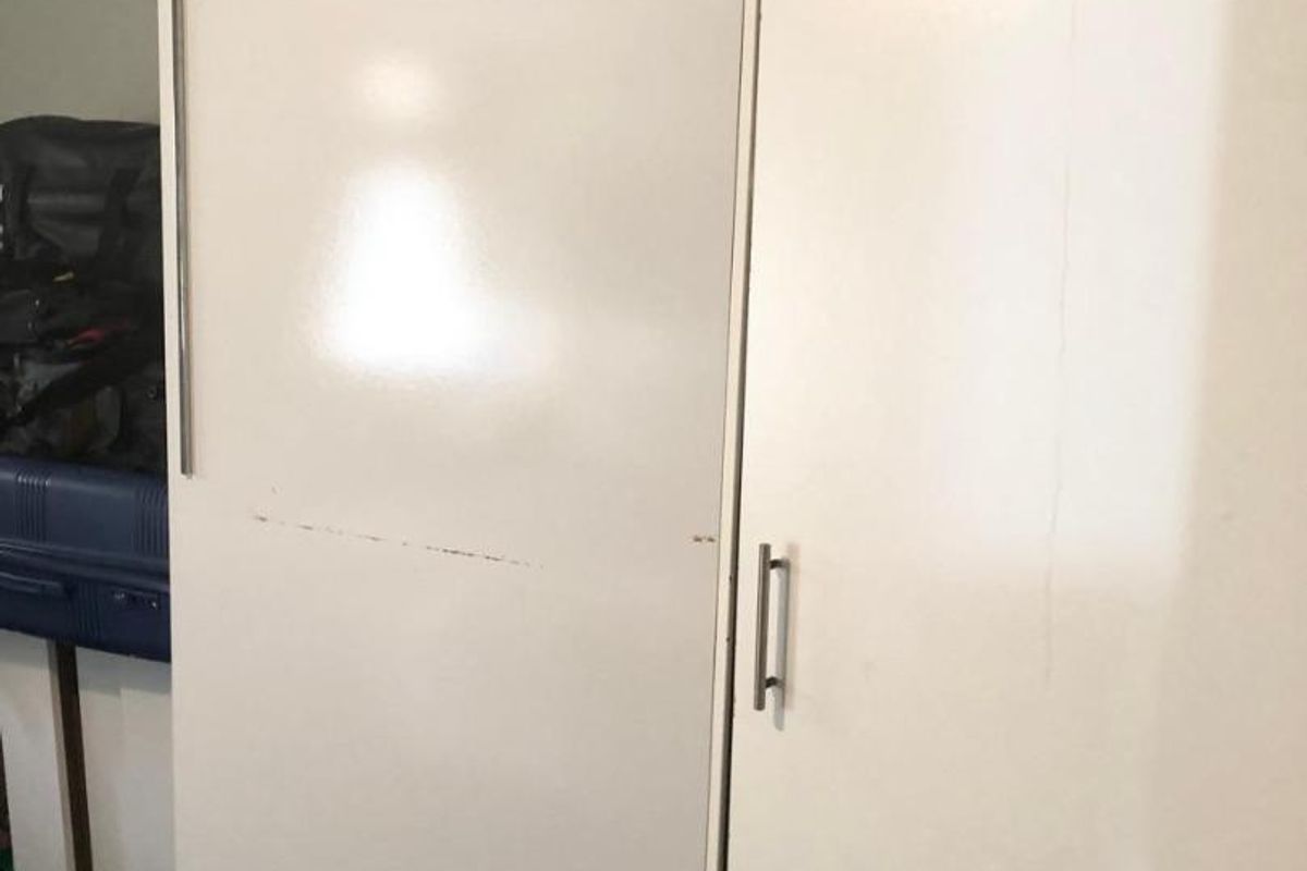 A bedroom featuring a white built-in wardrobe with visible wear and tear on the doors and surrounding ceiling trim.