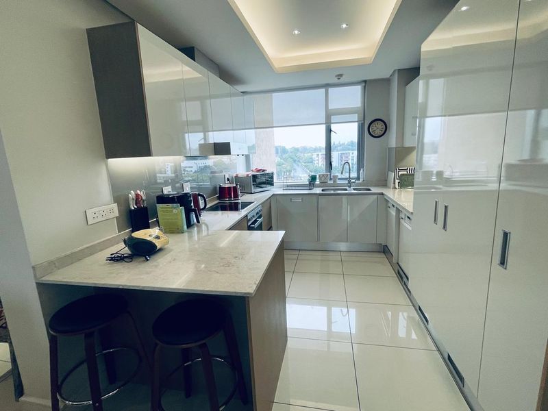 Modern kitchen featuring high-gloss cabinetry, stone countertops, integrated appliances, and a breakfast bar, complemented by recessed lighting and large format floor tiles.