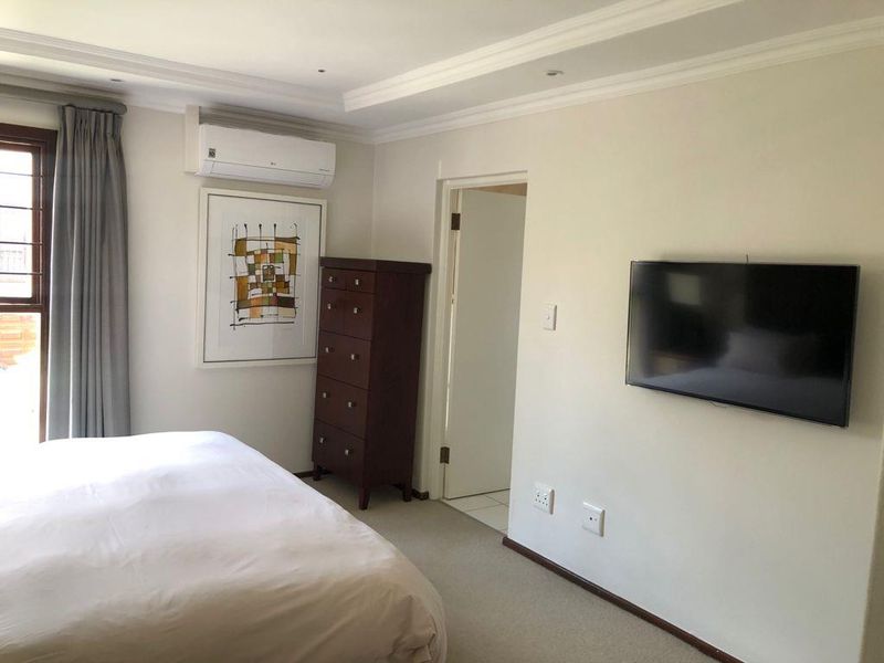 A well-maintained bedroom featuring neutral carpeting, recessed ceiling detailing, and a wall-mounted air conditioning unit.