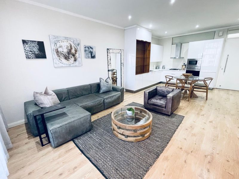 Modern open-plan living area featuring a sleek kitchen with built-in appliances, recessed lighting, and light wood-look flooring throughout.