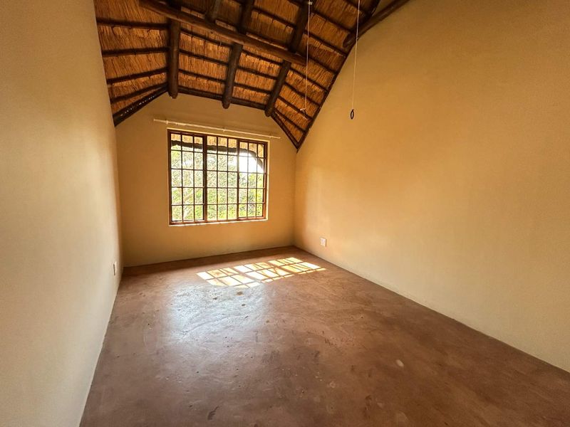 An empty bedroom featuring a high vaulted ceiling with exposed timber rafters, thatched roofing, and a large grid-pattern window.