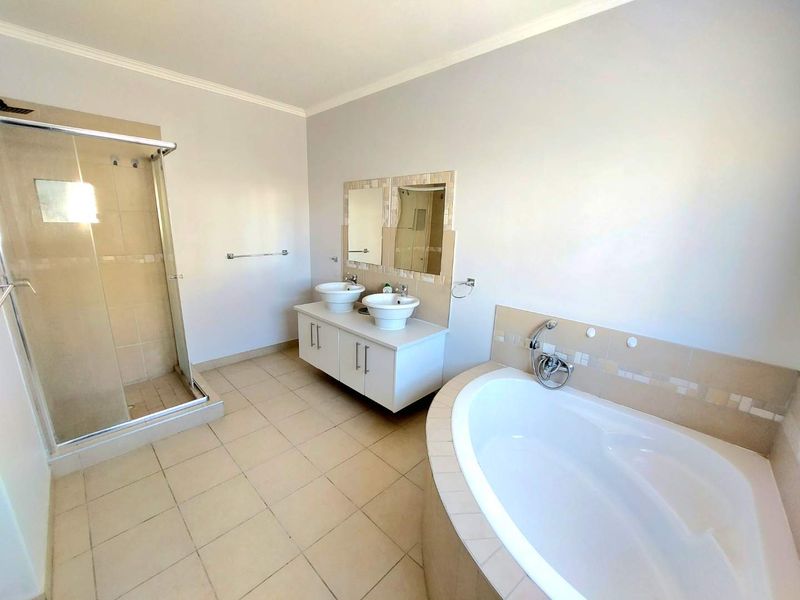 Spacious bathroom featuring a double vanity with vessel sinks, a built-in bathtub, and a separate glass-enclosed shower with neutral tiled finishes.