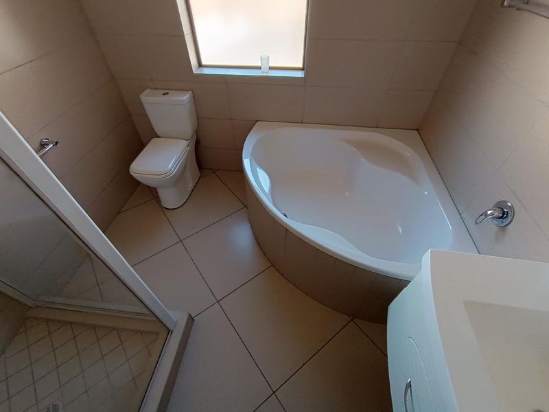 A clean, functional bathroom featuring a corner bathtub, separate shower enclosure, toilet, and vanity with tiled finishes throughout.