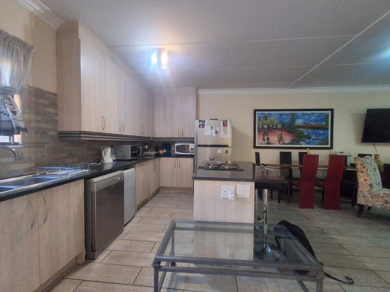 Open-plan kitchen and dining area featuring light wood cabinetry, granite countertops, a central island with a built-in hob, and tiled flooring throughout.