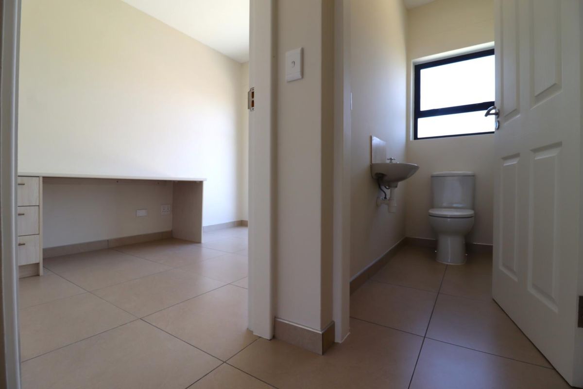 A functional bathroom featuring a wall-mounted basin and toilet, adjacent to a small room with a built-in desk area.