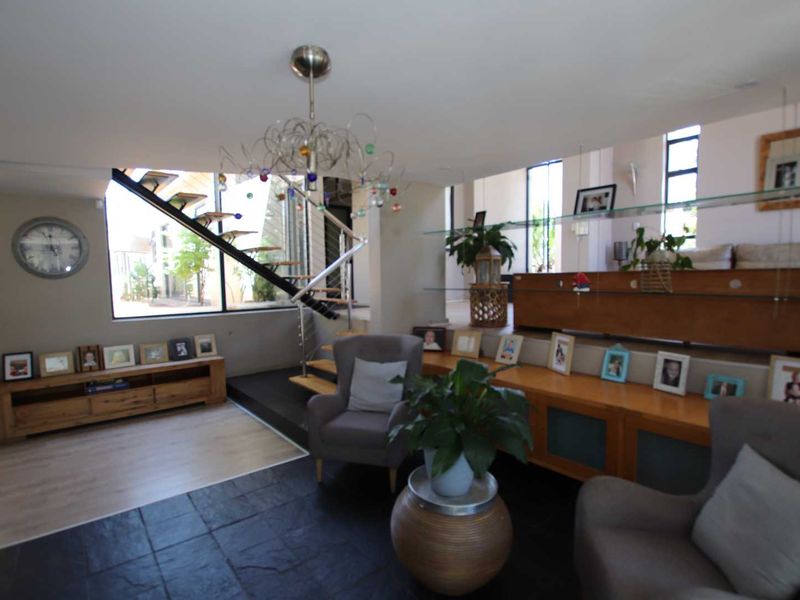 Spacious living area featuring a modern floating staircase, split-level flooring with slate and laminate finishes, and integrated glass shelving.